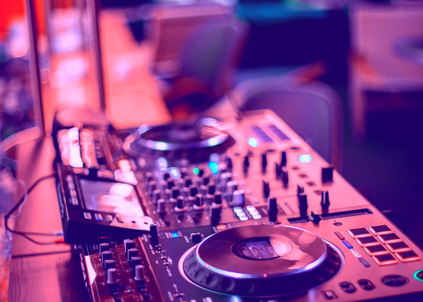 Close-up of a DJ mixer and turntables in violet light